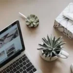 "A minimalist, high-angle flat lay photograph of a clean, modern digital marketing workspace. The desk features a laptop displaying marketing analytics charts, a premium notebook with an open pen, a cup of coffee, and small potted succulents. Soft, natural lighting creates an organized and professional atmosphere."